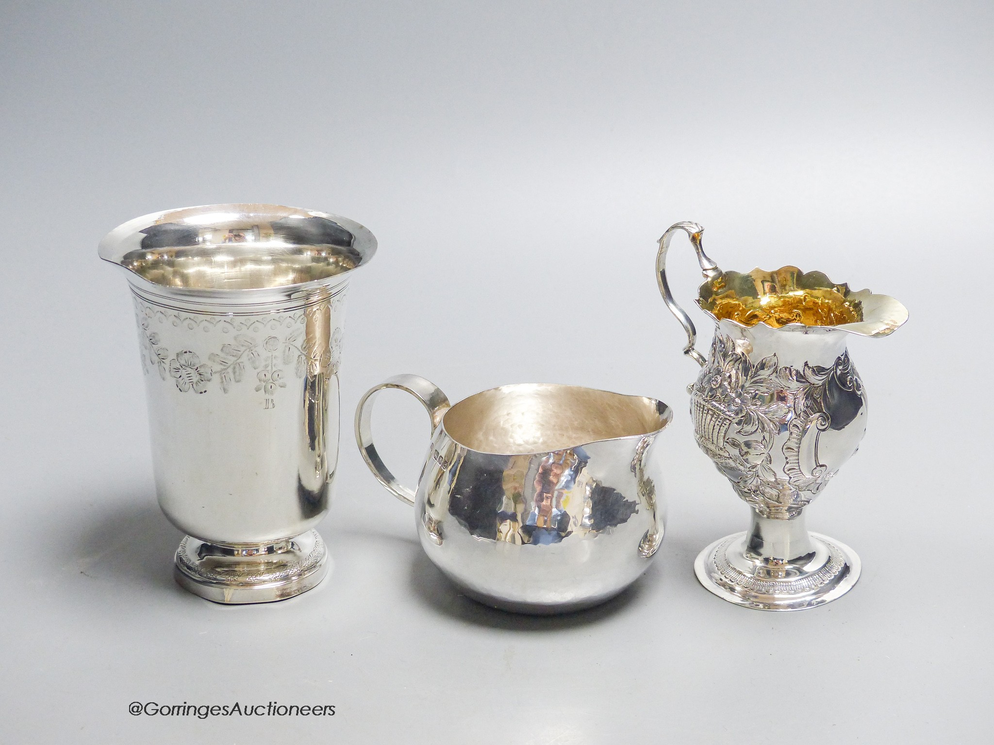 A George III later embossed silver cream jug with later base?, 11.5cm, a modern silver cream jug and a French white metal beaker, gross 10.5oz.